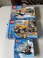 Four LEGO City boxes stacked, showing fire boat, dump truck, and excavator sets.