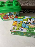 Photo showing LEGO Duplo 10945 Garbage Truck and Recycling set box and the large green LEGO block storage container behind it.