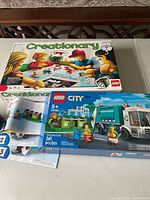 Photo showing boxed LEGO Creationary game and LEGO City 60386 Recycling Truck set with pieces and instructions.