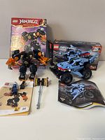 LEGO Technic Monster Jam Megalodon set built next to its box and instruction manual, along with LEGO Ninjago Cole’s Elemental Earth Mech built with some loose pieces and instructions.