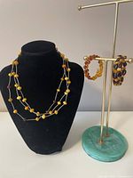 Two multi-strand Baltic amber beaded necklaces displayed on a black bust and two matching amber bracelets on a metal and stone stand. Shows beads colors and silver bead tarnishing.