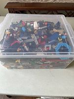 Clear plastic bin filled with mixed LEGO bricks and parts in various colors and shapes, viewed from top with lid on.