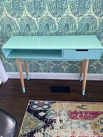 Full front view of the modern mint green glossy sideboard against patterned wallpaper, showing drawer and open shelf with wooden legs accented with mint green paint.