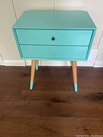 Front view of the turquoise wooden side table showing drawer and legs.