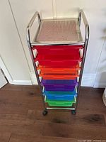 Front view showing metal frame and six plastic drawers in different colors with caster wheels.