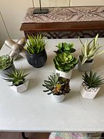 Full view of nine assorted artificial succulents and one silver metallic decorative object, showing varied pot shapes and leaf styles.