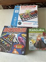 Photo showing Mastermind game box, KidzLabs Kitchen Science kit box with model volcano, and Snap Circuits Skill Builder box on table.