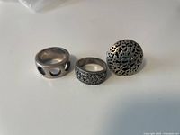 Photo showing three sterling silver rings with etched and pierced designs including a dome-shaped ring, wide band with geometric etching, and band with large holes.