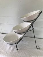 Side view of black metal 3-tier slanted rack holding three white ceramic bowls of varying sizes