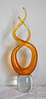 Full front view of amber coloured swirling abstract art glass sculpture on clear pedestal base