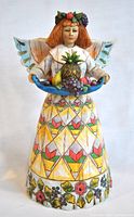 Front view of Angel of Generosity figurine showing colorful dress, fruit bowl, and facial details.