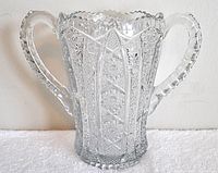 Front view of clear pressed glass container with two handles and detailed vertical panel pattern.