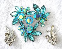 Aqua blue Aurora Borealis brooch and pair of clear rhinestone Sherman clip-on earrings laid on white background.