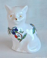 Front view showing the cat figurine with gold-painted eyes and nose, floral decorations on body.
