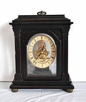 Front view of the dark wooden Bombay mantel clock showing the round clock face with Roman numerals and visible brass mechanism behind glass.