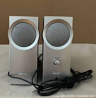 Pair of Bose Companion 2 computer speakers front view showing silver face panels, black plastic backs, volume control knob, and audio cable with 3.5mm plug.