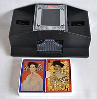 Top view of black Bicycle automatic card shuffler with two decks of Gustav Klimt playing cards laid in front.