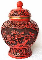 Front angle view showing detailed cinnabar carving of flowers and bird on red lacquered ginger jar with brass-lined rim and lid.