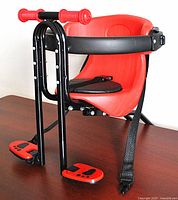 Red and black child's bike seat with molded plastic seat, black safety bar, padded base, and footrests