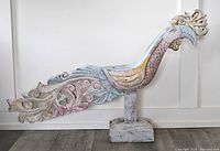 Side view of large hand carved wooden rooster in pastel colors, mounted on a wooden base, showing full profile including tail details.