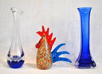 Full lot photo showing round base blue glass vase, multicoloured glass rooster and square based blue glass vase.