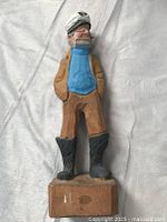 Front view of a hand-carved wooden sea captain sculpture standing on a wooden base, showing the painted details of the figure's clothing and face.