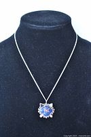 Pendant and chain displayed on a black neck jewelry stand showing front view of the pendant and chain.