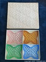 Top view of a set of four butterfly-shaped trinket dishes in pink, amber, green, and blue colors inside a textured white box.