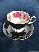 Tea cup and saucer showing Old English Rose pink roses on matte black background with gold rim and detailed handle