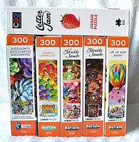 Side view of five Buffalo brand 300-piece puzzles including Succulents, Rainbow Umbrellas, two Adorable Animals and Up Up and Away hot air balloons.