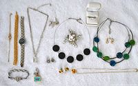 Photo showing all jewelry items laid out on white fabric including necklaces, bracelets, earrings, brooch, charm, watch, ring, and cuff-links.