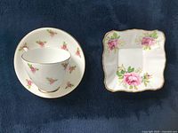 Top view of Gladstone Pink Rosebuds tea cup and saucer alongside Royal Albert American Beauty Rosebud candy dish displaying floral patterns and gold rims