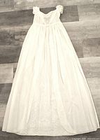 Full view of long vintage cotton christening gown laid flat on wooden floor showing length, lace hem, and gathered bodice.