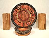 Front view of hand painted wooden Peruvian plate with geometric designs, two rectangular wooden candle holders, and live edge wooden glass holder.