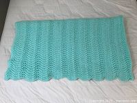 Mint green crocheted afghan folded and laid flat on a white surface showing texture and scalloped edges.