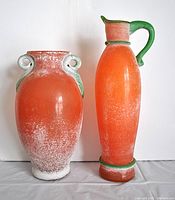 Full view of the orange blown glass vase and pitcher side by side showing their shapes and colors.