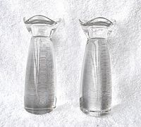 Pair of crystal clear art glass candle holders placed on a white textured background showing front and side views