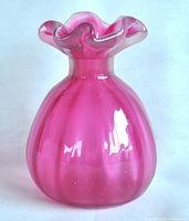 Front view of a ribbed pink glass bud vase with a ruffled top.
