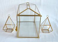 Photo showing two pyramid-shaped planters flanking the rectangular glass hot house with brass frame and lock.