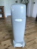 Front view of white Playtex Diaper Genie Complete diaper pail on wood floor showing pedal and locking button.