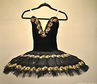 Front view of black ballet tutu with gold and black embroidered lace featuring jewel embellishments, cream elastic shoulder straps, and full tutu skirt with lace trim and rhinestones.