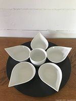 Top view of assembled black wooden lazy Susan base with five white petal-shaped dishes and one central circular dish placed on top, showing the arrangement and size.