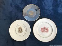 Photo of three collector plates showing Queen Elizabeth II Silver Jubilee and commemorative designs on a blue background.