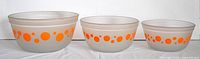 Set of three nested vintage mixing bowls with orange dots on frosted glass.