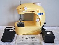 Front view of the yellow Sew Cute sewing machine with foot pedal, power cord, and manual spread in front