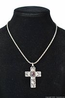 Full view of silver cross pendant with garnet on chain displayed on black velvet stand.