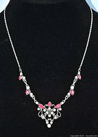 Full view of sterling silver lavaliere necklace on black stand showing chain, rubies, and pearl accents