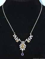 Full view of the necklace displayed on black fabric, showing overall design and elements including citrines, amethysts, and pearls.