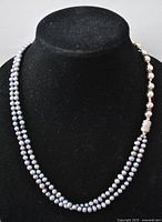 Full view of the necklace on a black display showing the double strand of peacock pearls and silver beads.