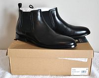 Pair of black leather Steve Madden Duke boots size 11 positioned on and beside their cardboard box with label